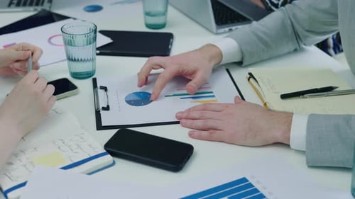 Hands of the Group Discussing Income Charts and Graphs on the Paper Notebook