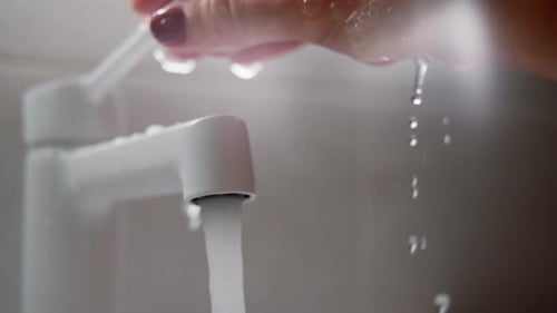 Closeup of a Modern White Faucet Running As a Hand with Red Nail Polish Rinses Beneath the Stream