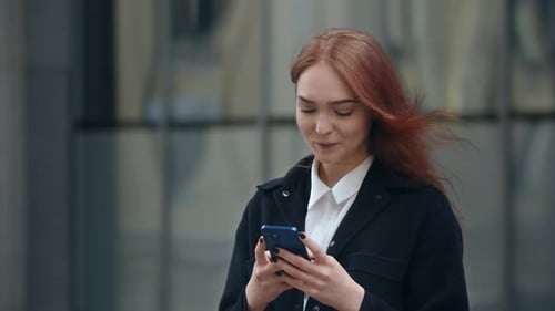 Ginger Young Woman is Smiling While Reading Message on the Street Smiling Girl with Smartphone