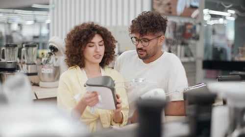Young couple choosing hand mixer in electronics store in slow motion