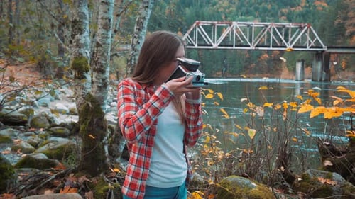 Photographer woman takes Polaroid photo along riverside among fall colors