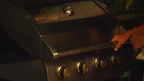 Man Operating Outdoor Gas Grill with Closed Lid During Nighttime