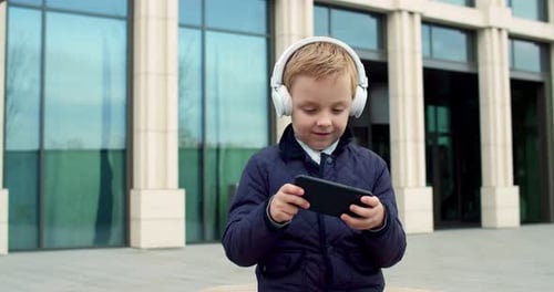 Boy with Headphones Using Smartphone Outside Building