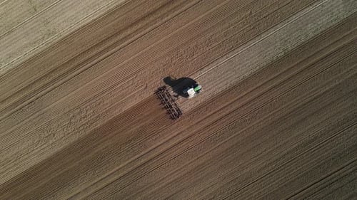 An aerial view of a tractor working on a large agricultural field, plowing the soil in straight, par