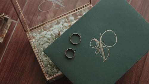 wedding rings resting on green monogrammed envelope beside floral glass box