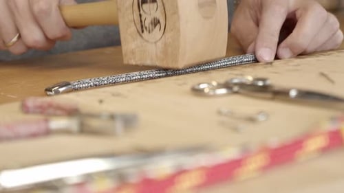 Skillful craftsman straightening freshly made bracelet with wooden hammer