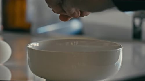 Öffnen Sie das rohe Ei mit den Händen in eine weiße Schüssel, um das Frühstück zuzubereiten.