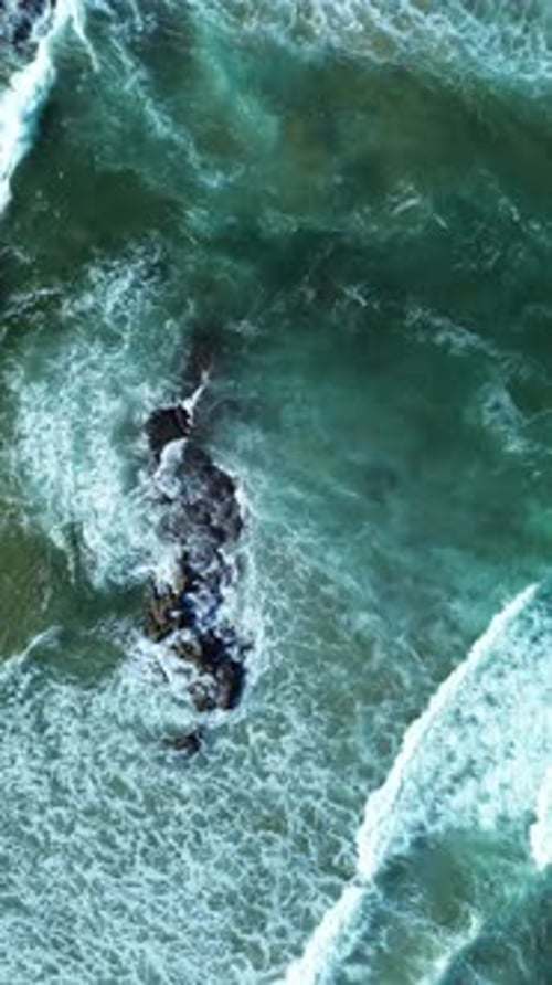 Small waves breaking against rocks aerial top view