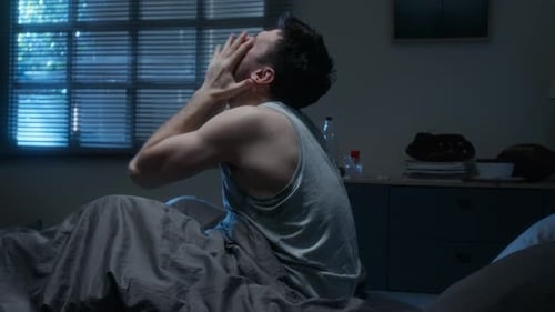Homme assis dans son lit la nuit et hurlant d'insomnie