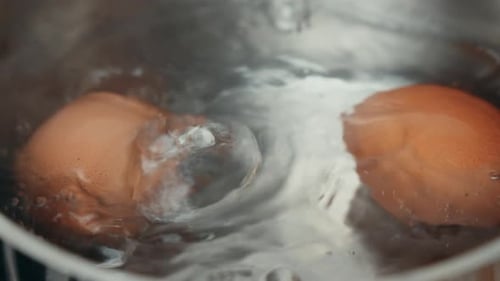 Zwei Eier, die in Wasser auf einem Herdtopf kochen.