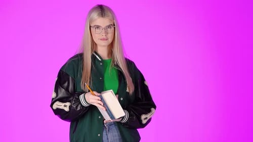 Young Blonde Student Enjoying Reading a Book and Smiling, Studio Portrait With Pink Background
