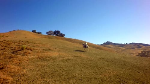 Cowboy On Horseback Traveling On Mountain Range On Sunny Day Slow Motion 2