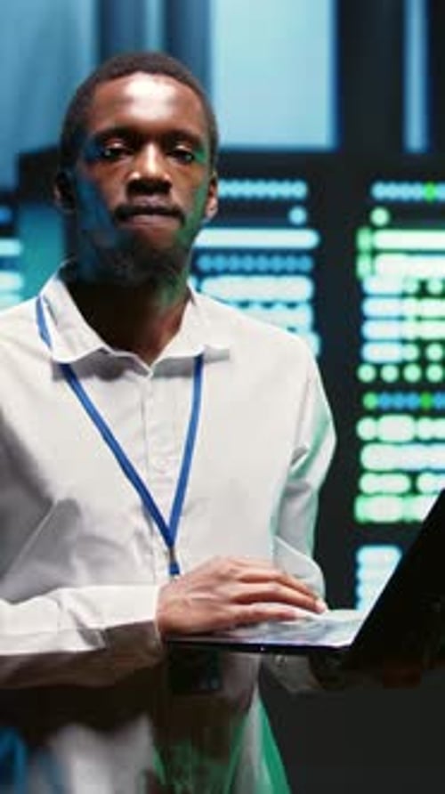 Man Types On Laptop in Front of Servers