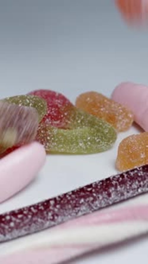 A vast variety of gummy candies in different colors and shapes fall onto the table, in slow motion.