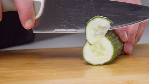 The Hands of a Man Cut a Cucumber with a Knife on a Board