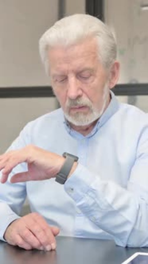 Thoughtful senior man looking at smartwatch in workplace