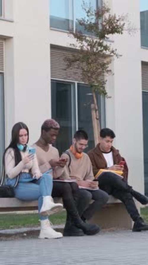 Mulitcultural Students Using Their Own Mobile Sitting in a Bench Outdoors