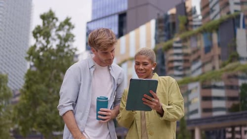Young Adults Look at Tablet Together in City Park