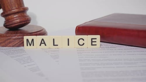 Word Malice Spelled Out Next to Gavel and Book