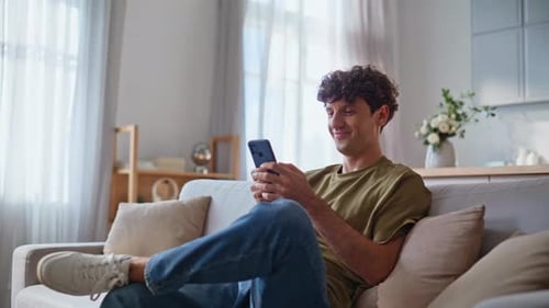 Man Relaxing on Couch Using Smartphone at Home