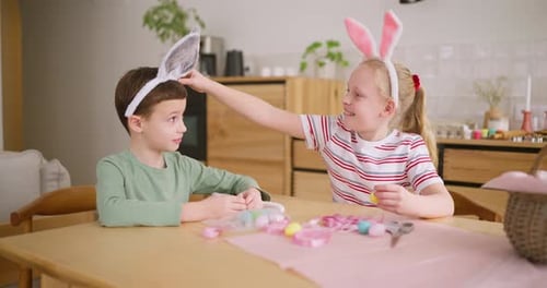 Two Children Decorate Easter Eggs at Table
