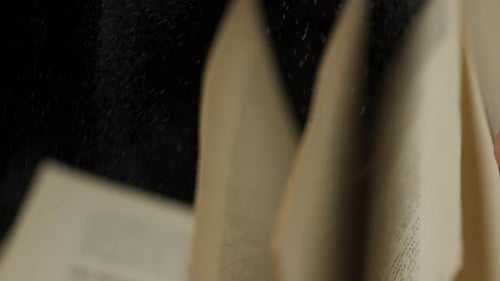 Close Up Studio Shot of Old Retro Hardcover Book on Dark Background in Warm Light Man Hand Flipping