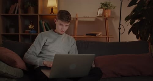 Man Works on Laptop on Couch at Night