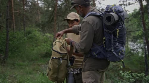 Caring Indian Father Helping Son Put on Backpack after Resting in Forest
