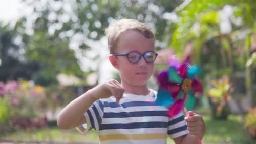 Boy in glasses is playing with pinwheel in a garden