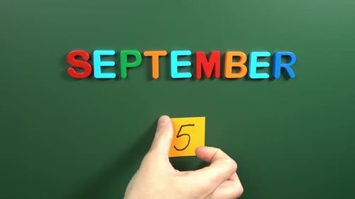 Hand sticking a sticker 5 September calendar day on school board. 5 date of September. Fifth day