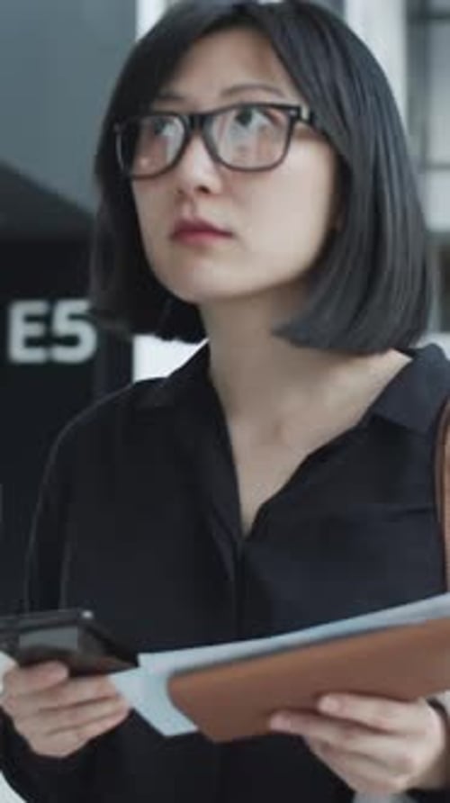 Asian Woman Anxiously Checking Documents in Busy Modern Airport