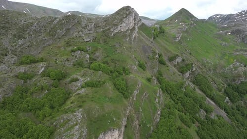 Flying over beautiful green mountains. Panorama of mountains and alpine houses below. Aerial view.
