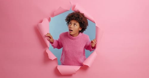 Surprised woman looks through torn paper background