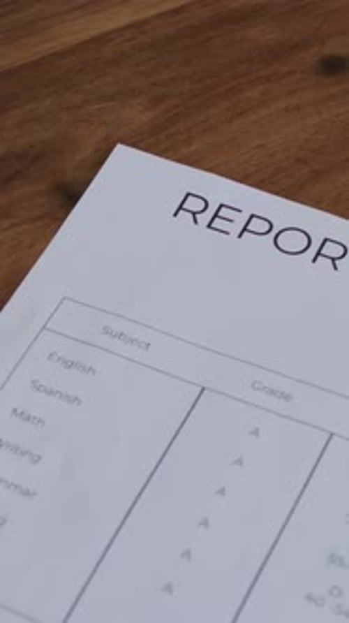 Vertical video: Panning camera revealing report card, showing letter A+ on wooden table, plant left