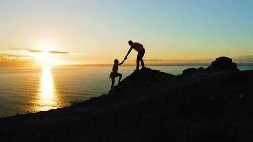 Couple of Travelers Climb the Mountain During Sunset and Look at Ocean Sunset