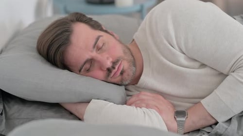 Müder junger Mann schläft, während er auf der Seite im Bett liegt