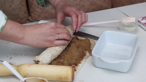 Zubereitung von Zimtstangen. Eine Frau rollt ausgerollten Zimtteig auf. Die Kamera bewegt sich auf einem Slider