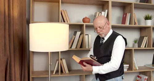 Älterer Mann in einer Weste liest im Wohnzimmer