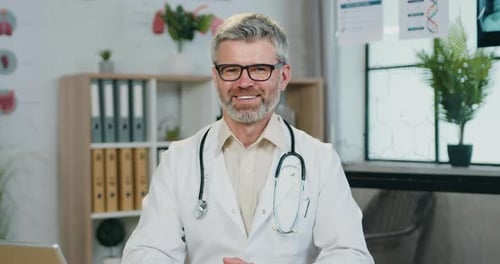 Portrait of doctor in glasses which looking into camera with satisfied face expression on clinic