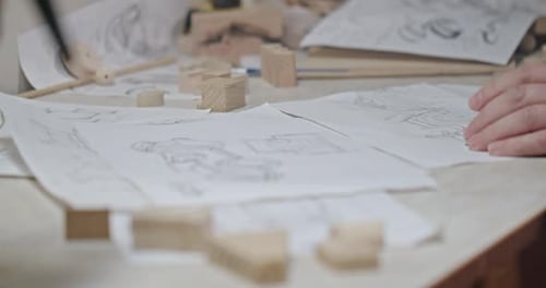 A Man Draws Drawings in His Small Bright Workshop Creates a Sketch of Wooden Eco Toys and Makes