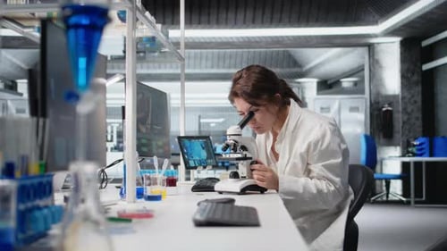 Scientist Woman Uses Microscope in Lab, Male Researcher
