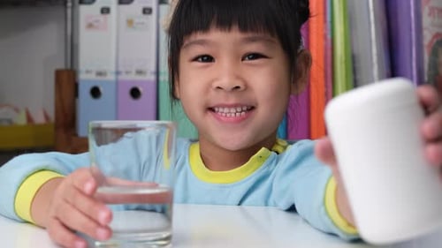 Smiling Child Holding Glass of Water at Table