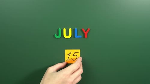 Hand sticking a sticker 15 July calendar day on school board. 15 date of July. Fifteenth day