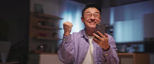 Man Celebrating Success While Using Smartphone Indoors