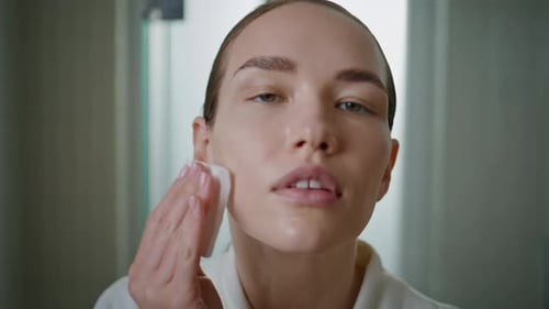 Woman Cleansing Face with Cotton Pad in Bathroom