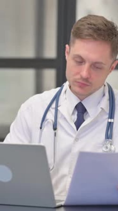Vidéo verticale, médecin de sexe masculin travaillant sur des documents médicaux et un ordinateur portable