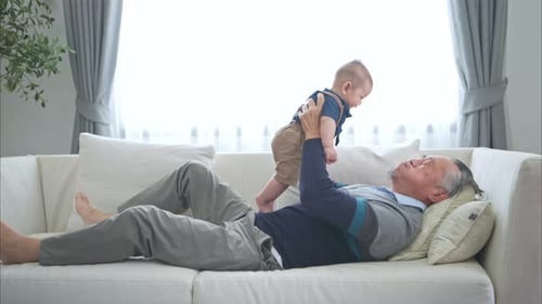 Ein winziges Enkelkind, das glücklich mit dem Großvater auf der Couch im Wohnzimmer lächelt