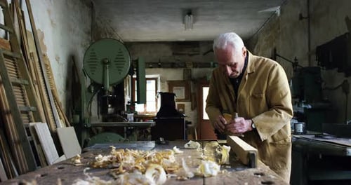 Gray Haired Man Uses Tool On Wood in Workshop