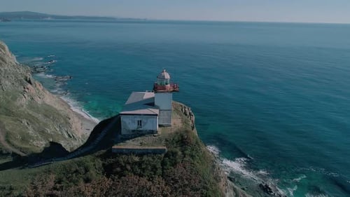 Panoramaaufnahme des weißen Leuchtturms auf der felsigen Klippe am Meer. Wellen stürzen auf den