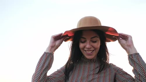 Smiling Woman Puts on Hat at Sunset